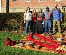 five individuals stand outside of Martin Hall in front of a blanket with the ties for the Peace Tree
